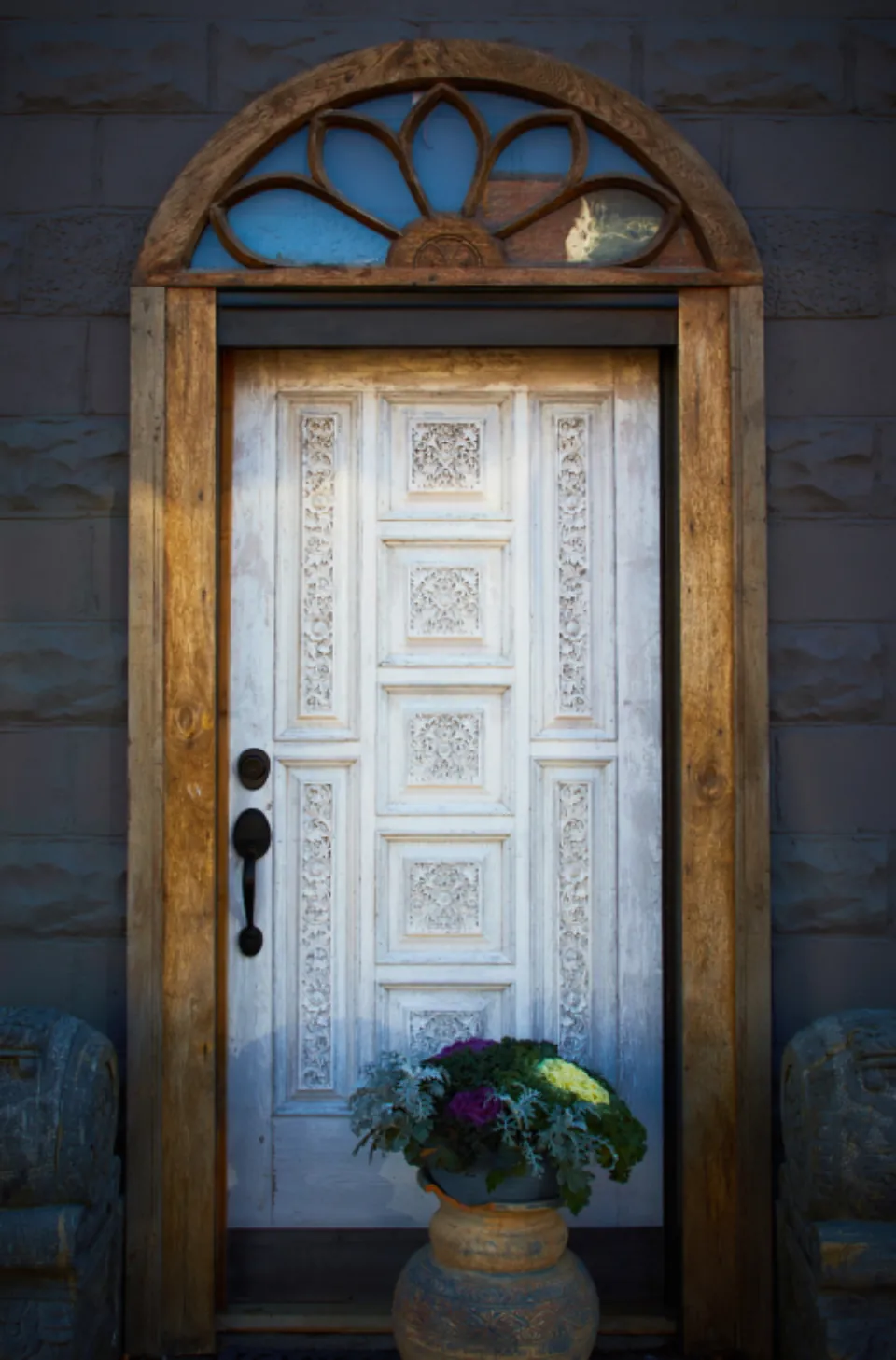 A white front door with a wooden arched frame and a flower planter