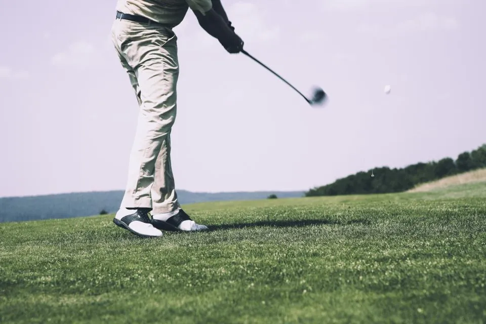 A golfer mid swing on a green fairway