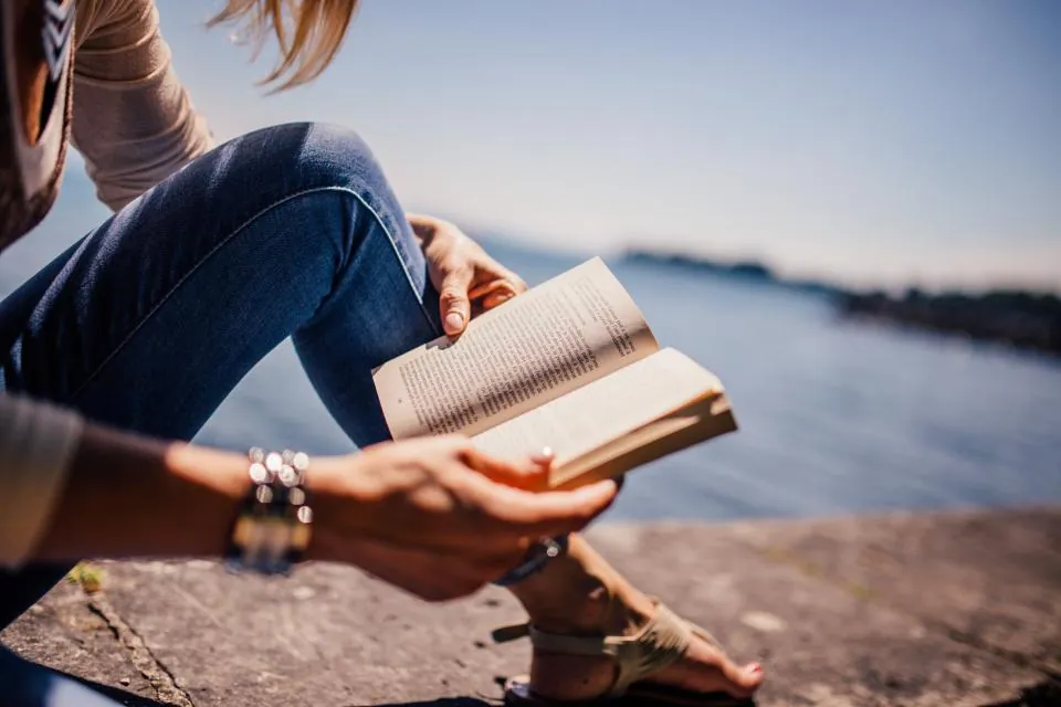 A person reading a book outside by the water